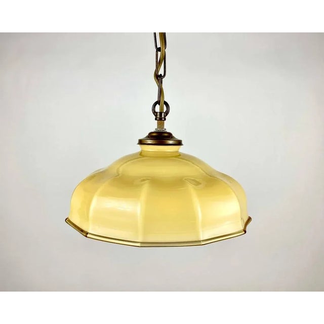 Yellow glass hanging lamp with brass fixture from the 1960s. The glass shade has a bit of the shape of an umbrella....