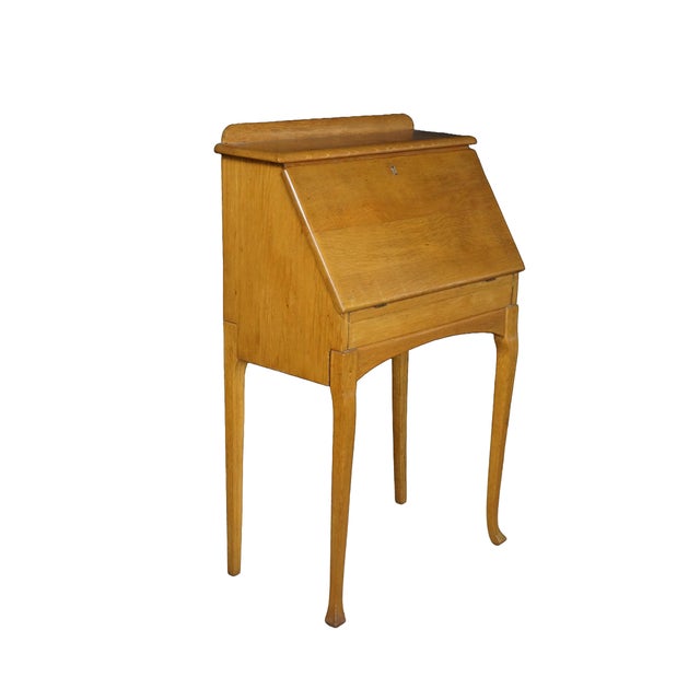 This antique oak slant-front bureau desk opens to reveal a clean and organized interior workspace featuring a built-in...