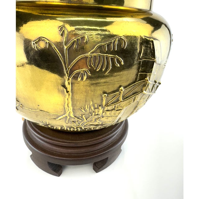 A sculptural mid-century brass table lamp featuring a richly embossed Chinoiserie landscape with pagoda, bridge, and tree...