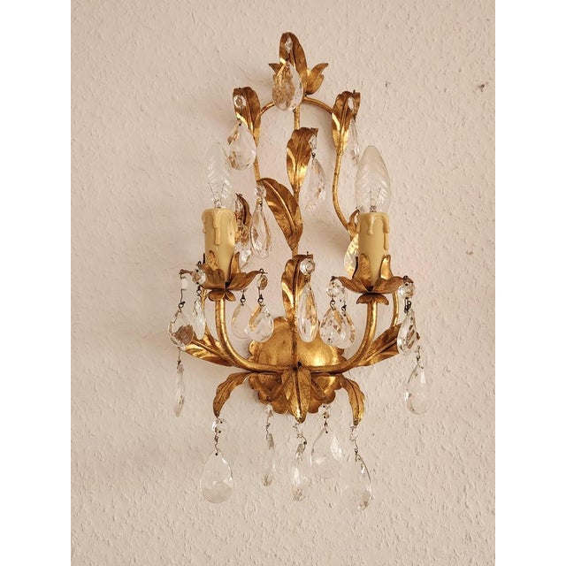 A highly decorative, hand-forged wall sconce, gilded in gold leaf with floral and leaf embellishments and crystal drops. a...