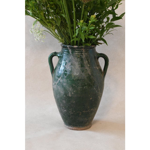 This handled Mediterranean vase features a warm terracotta finish with a darker, textured glaze around the neck and...