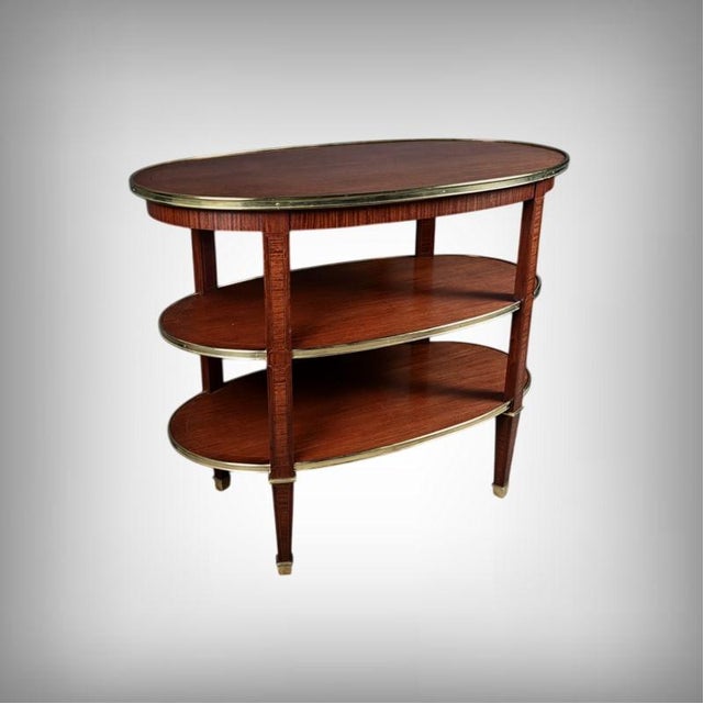 An elegant oval side table with three tiers, crafted in mahogany in the Louis XVI style. Each tier is edged with a finely...
