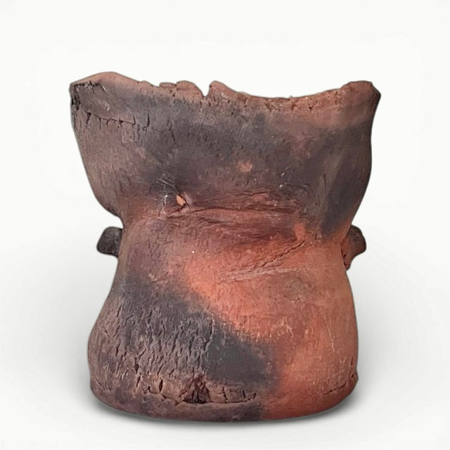 A petite pit-fired studio pottery vase of slightly twisted form in earthy tones of terracotta and ash. Two little arms...