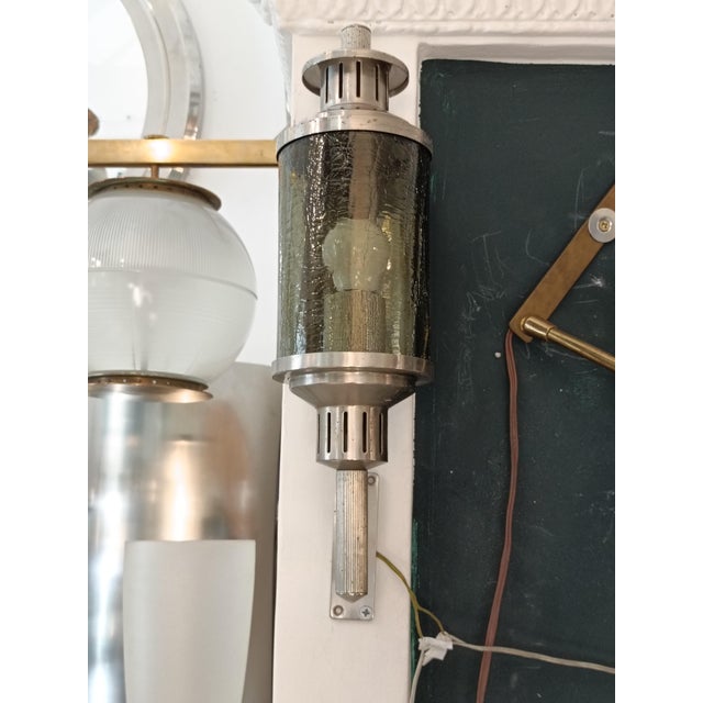 A lantern-style wall lamp with a strong vintage and industrial feel. It stands out for its central body made of thick,...