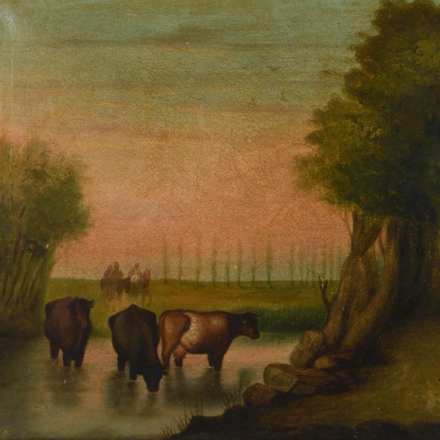 This Antique Framed Cattle Watering Oil on Canvas Painting depicts a peaceful pastoral scene where a farmer takes a moment...