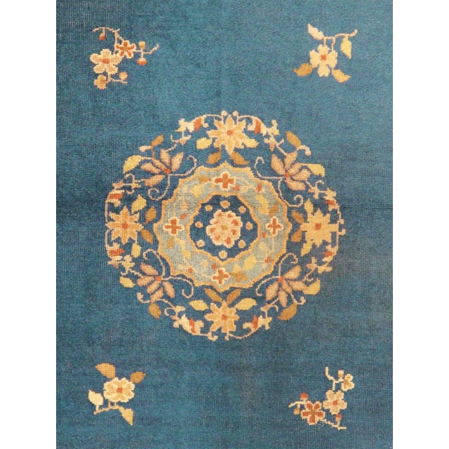 An antique Chinese Peking rug featuring a soft blue field with a central floral medallion, scattered floral sprays, and...