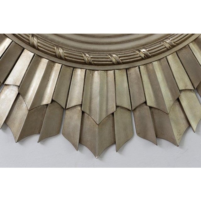 This is a dramatic contemporary sunburst mirror featuring a bold circular frame with radiating hand-carved rays finished...