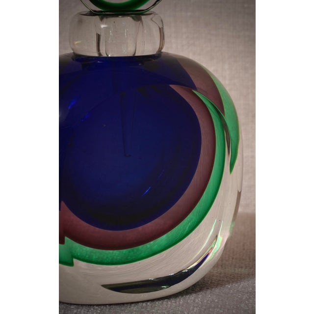 A perfume bottle with internal decorations in various shades of blue, green, and transparent. A sculpture of the highest...