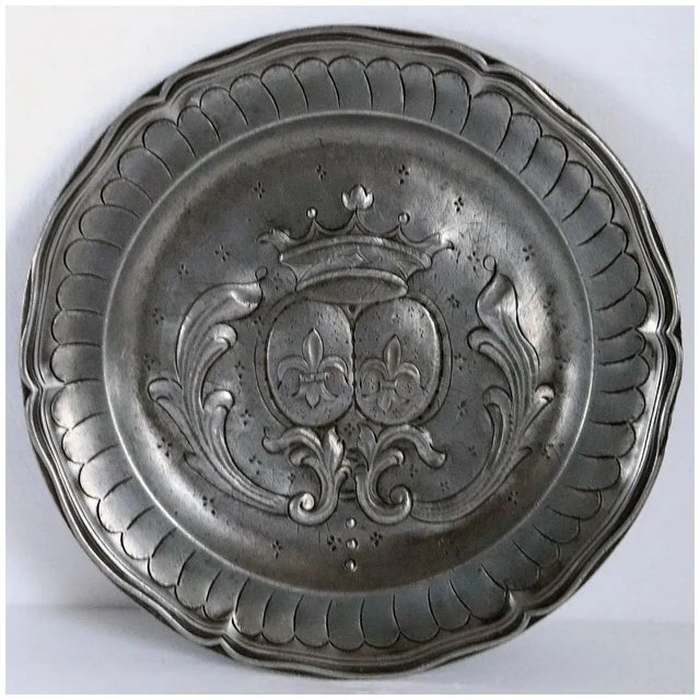 An antique round plate with a wide rim with a wavy and reeded edge. The center with double. oval coat of arms with fleur-...