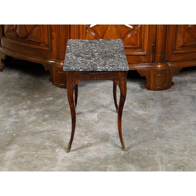 A French Louis XV style walnut side table from the 19th century, with grey marble top and bronze feet. Created in France...