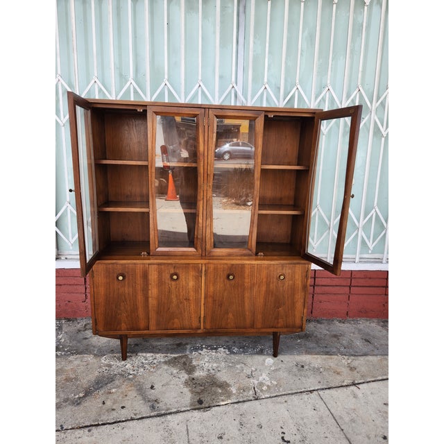 Vintage walnut china cabinet has a two-piece design with a glass-front upper hutch and a solid wood lower sideboard. The...