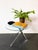 A round glass side table with a sculptural chrome-finished metal base, characterised by its minimalist modern design and...