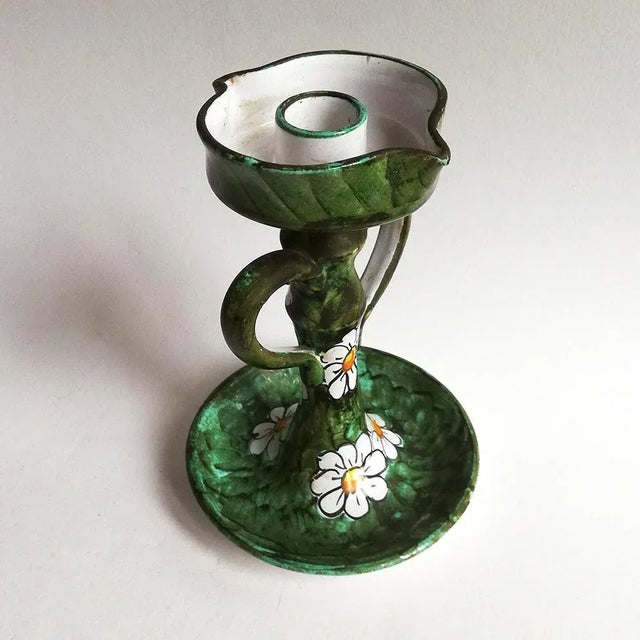 This ceramic candle holder is colored white and yellow with a green base. It features a daisy decoration in terracotta at...