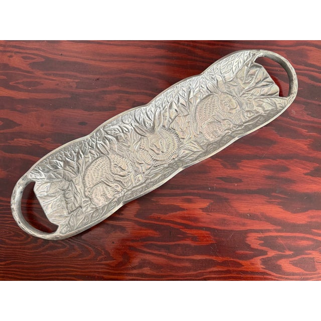 Long cast aluminum serving tray with rabbits among raised leaves and flowers. Open handles at each end. The metal has a...