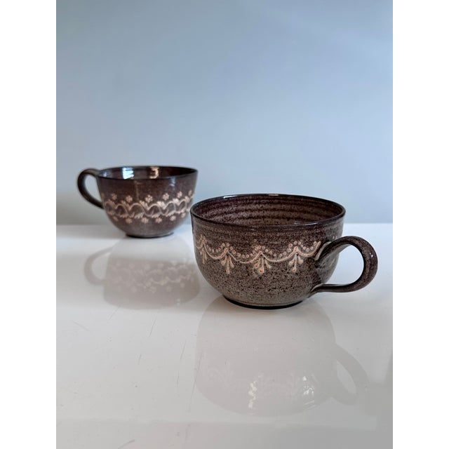 Handcrafted ceramic mugs from the Serocka workshop, decorated with delicate light lines and dots on a dark brown body. The...