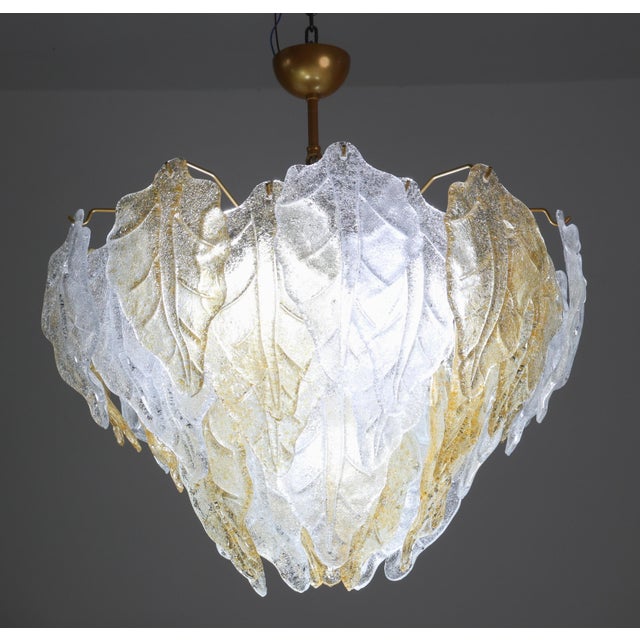 A stunning Murano glass chandelier featuring dozens of alternating leaves in clear and orange glass. The chandelier...
