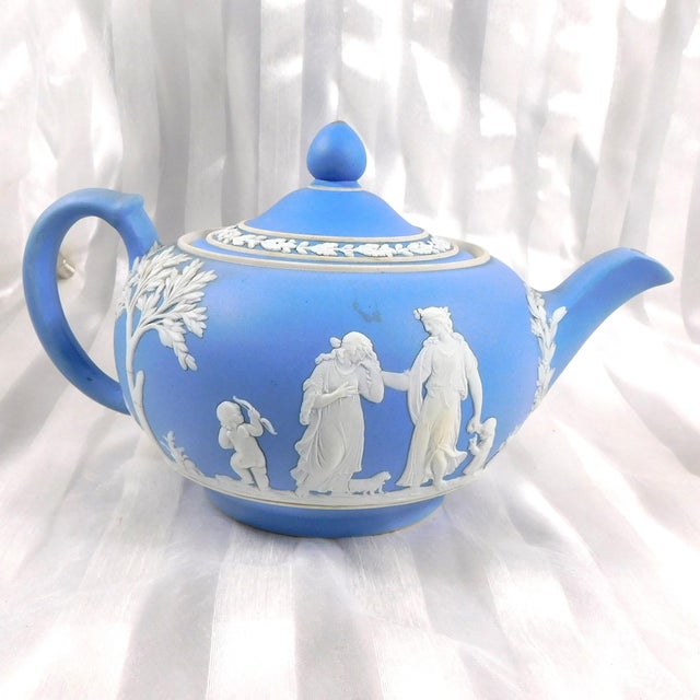 This is a light blue Wedgwood Jasperware teapot in an unknown pattern. The teapot has a white design of women and children...