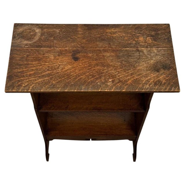 A charming early 20th-century English side table and bookcase in the Arts and Crafts tradition, finely crafted from oak...