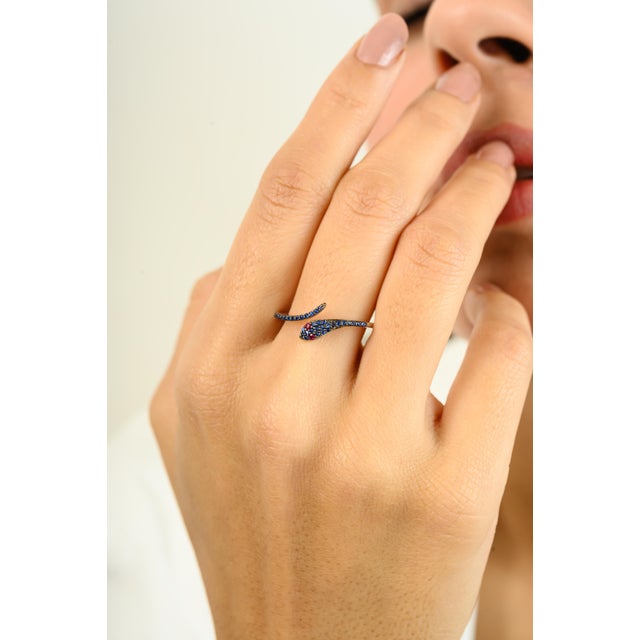 This Art Deco Red Ruby Eye Pave Blue Sapphire Thin Snake Ring in 18k White Gold featuring natural ruby blue sapphire of...