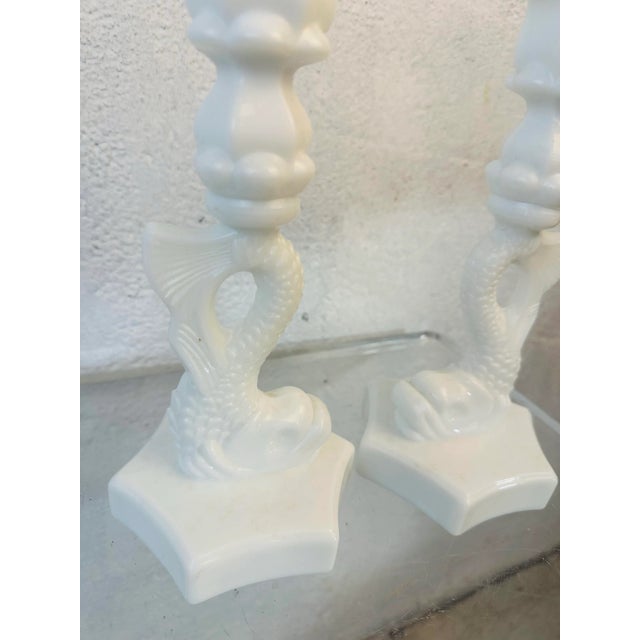 This is a pair of vintage milk glass candlestick holders designed in the form of stylized fish—likely dolphins—rising up...
