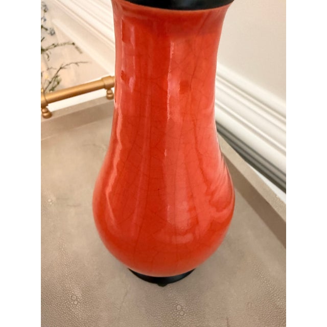 Decorative ceramic vase featuring a vibrant coral-orange crackle glaze with contrasting matte black neck and base details....