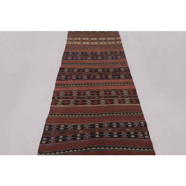 Made with handwoven wool circa 1950-1960, this 3x13 vintage Kilim runner enjoys complex horizontal band and tribal...