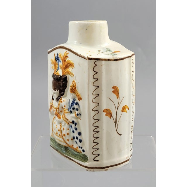 An English pearlware tea caddy dating to circa 1790–1800, decorated with moulded relief figures painted in underglaze...
