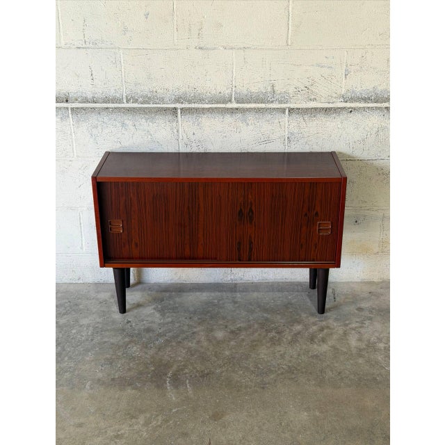 This compact sideboard features a clean-lined profile resting on tapered legs. Smooth sliding doors reveal open interior...