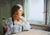 In "Missing You," a young woman gazes thoughtfully out of a window, her expression tinged with longing and introspection....