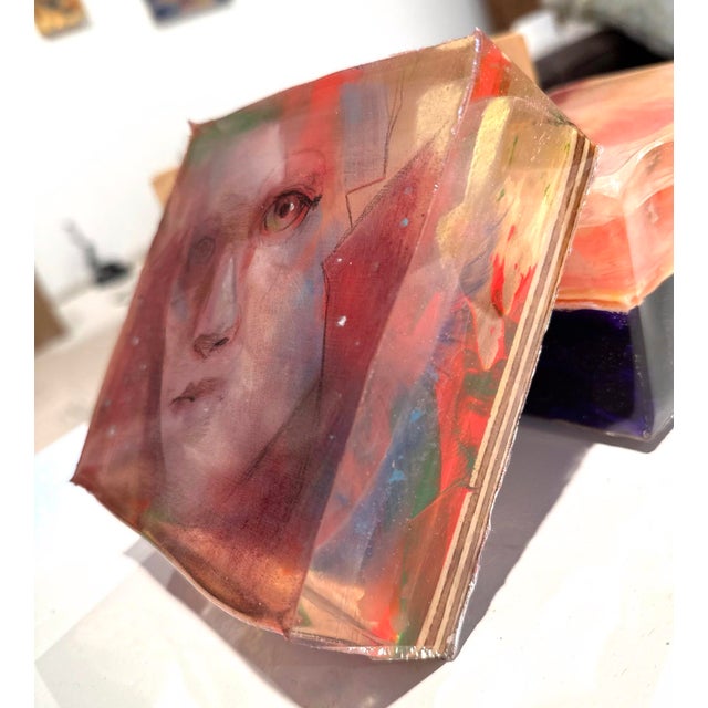 This artwork features a hauntingly expressive face, rendered with a delicate interplay of layered resin, pastel, and...