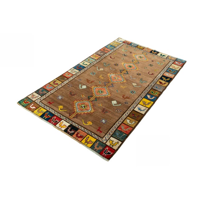 This expressive, hand-knotted vintage Gabbeh impresses with its warm color palette, variety of symbolic motifs, and...