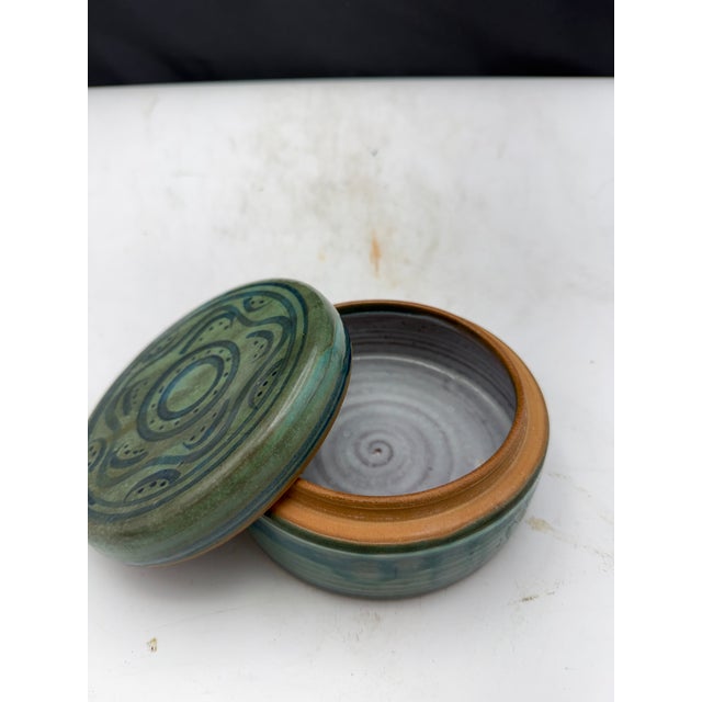 Handmade earthenware lidded box featuring a green glaze with abstract decorative patterns on the lid. The interior is...