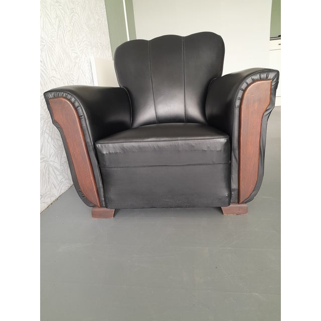 An elegant Art Deco style armchair, upholstered in black leatherette with distinctive wooden arm details. The chair...