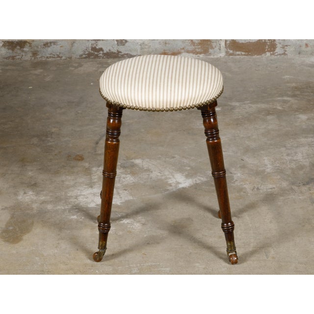 An English Victorian period oak stool from the 19th century with oval upholstered seat, turned legs resting on casters....