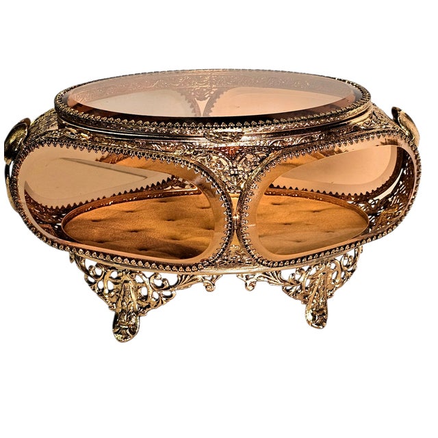 A mid-20th century ormolu jewelry casket featuring beveled glass panels and ornate Regency-style filigree metalwork. This...