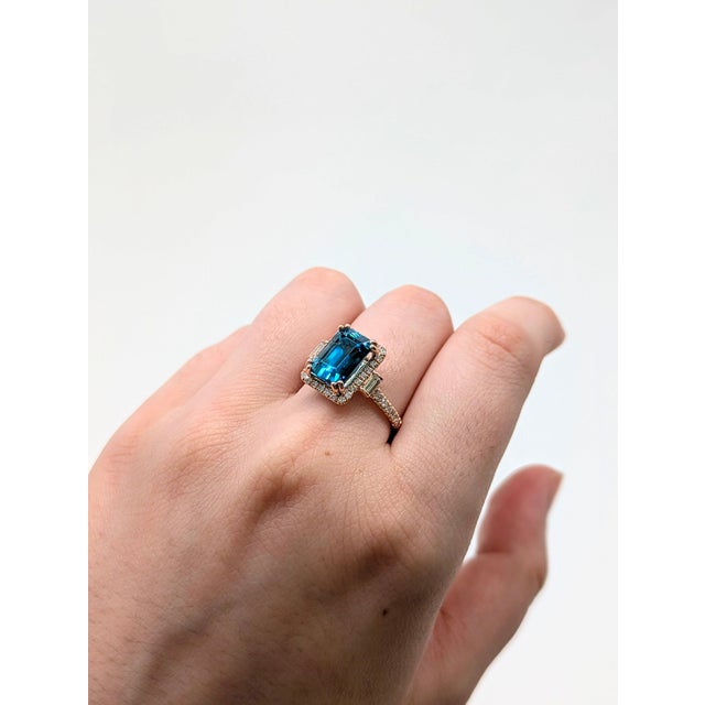 A blue zircon rests in a brilliant electric blue at the heart of this solid 14K rose gold ring, framed by forty-two earth-...