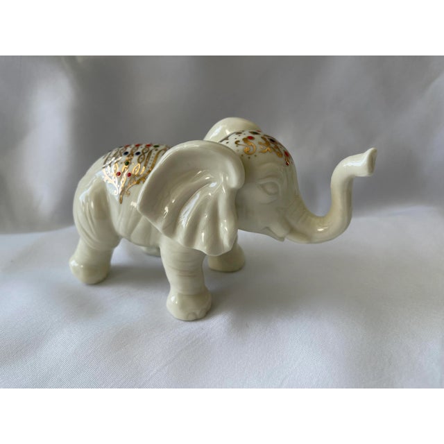 Vintage ceramic white elephant figurine with gold gilt designs on its head and back. The colorful placement of blue, red...