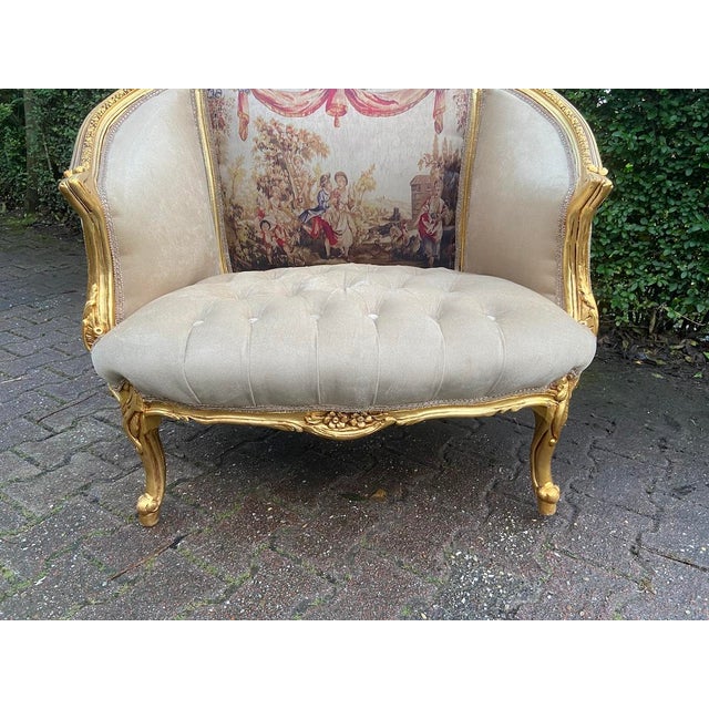 An elegant circa 1900 French Marquise loveseat, crafted from solid beechwood with a gilded gold finish, tufted beige...