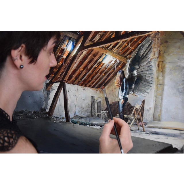 This oil on panel artwork depicts a solitary figure with ethereal wings standing in a dilapidated attic, bathed in soft,...