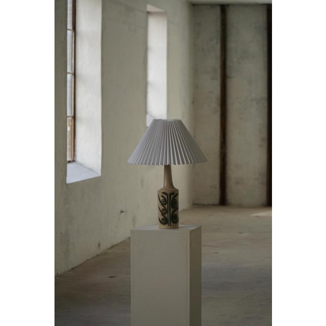 A danish stoneware table lamp by okela, produced during the 1960s. The lamp features a slender cylindrical form decorated...