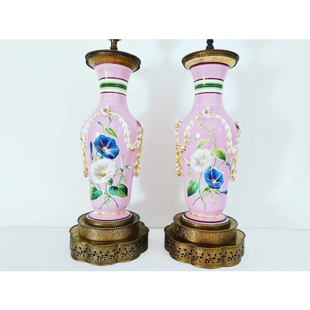 Gorgeous pair of French porcelain pink urn lamps painted with colorful morning glories, stripes, and gilded dimensional...