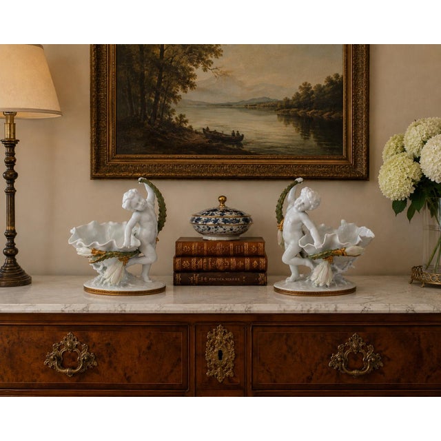 A remarkable pair of early-20th-century German porcelain compotes, each modeled with a sculptural putto supporting a...
