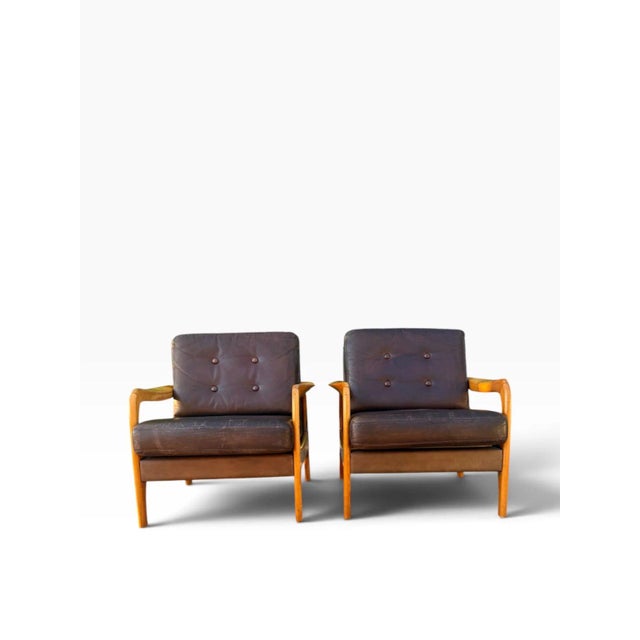 OVERVIEW A matched pair of mid-century Danish modern lounge chairs in brown leather on sculpted maple frames. Their broad...