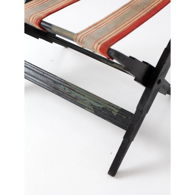 Vintage folding luggage rack dating from the 1920s–1940s with black painted wood frame and striped canvas webbing. Stepped...