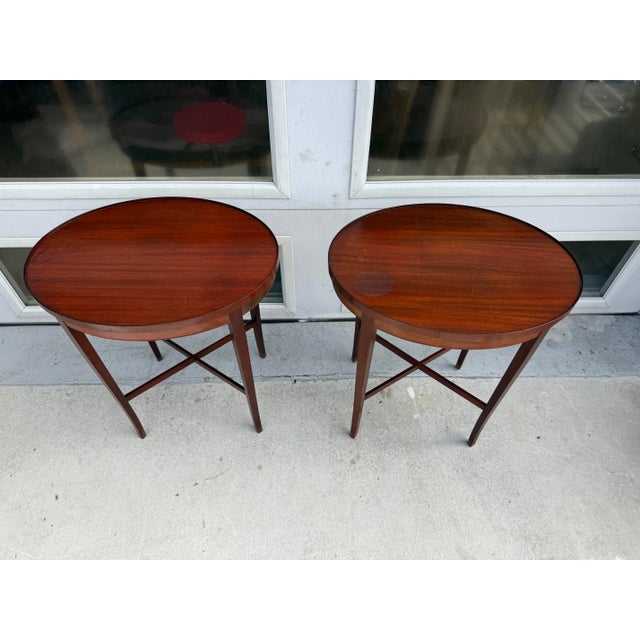 Beautiful pair of vintage wooden side tables featuring an elegant oval tabletop and slender tapered legs connected by...