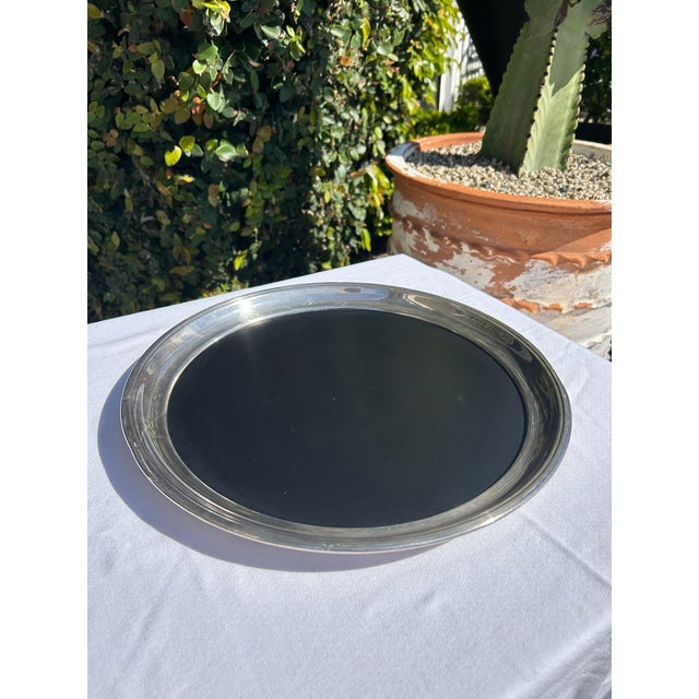 Vintage round serving tray featuring a silver plate rim with inset black resin center. The contrast between polished...