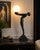 A dramatic late 20th-century Art Deco Revival figural table lamp featuring a stylized nude female figure gracefully posing...