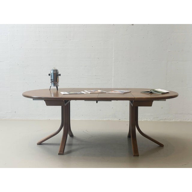 The round dining table by Dietiker is made of wood and features a striking, curved base. The warm, medium-brown color...