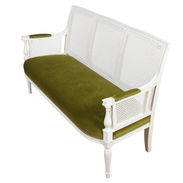 A Louis XVI style cane settee featuring a beautifully carved and painted white wood frame with three paneled woven cane...