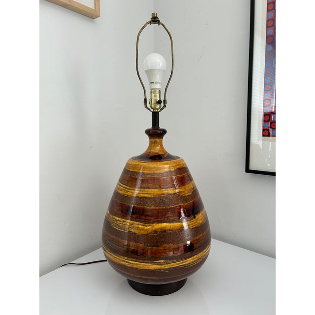 A Mid-Century Modern "Onion" pottery lamp in a striped patterned lava drip glaze in warm amber and brown tones. The smooth...